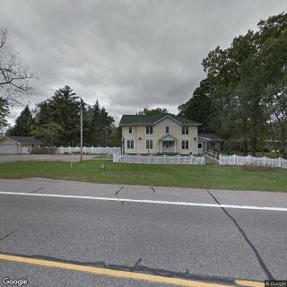 A suburban house with a white fence located near a road lined with trees.