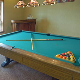 A billiards table set up with a cue stick and balls in a cozy game room.