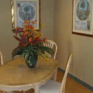 A dining area featuring a wooden table with a vibrant flower arrangement, surrounded by chairs and decorated with framed artwork on the walls.
