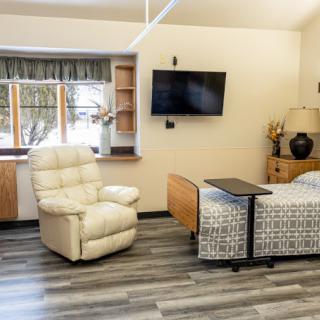 A cozy living space featuring a recliner, bed, wall-mounted television, and window with a scenic view.