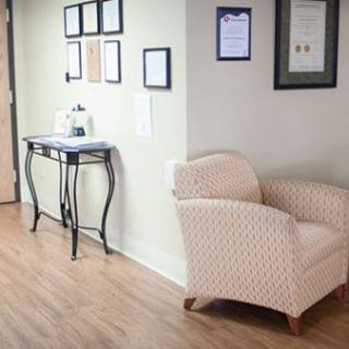 A cozy waiting room with a comfortable chair and framed certificates on the wall.