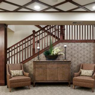 A cozy interior with a wooden staircase, two upholstered chairs, and a decorative cabinet.