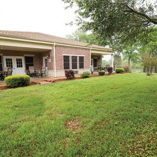A view of a brick house with a well-maintained backyard and patio area.