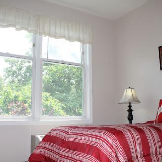 A cozy bedroom featuring a striped red and white bedding set, a bedside lamp, and a bright window offering a view of the greenery outside.