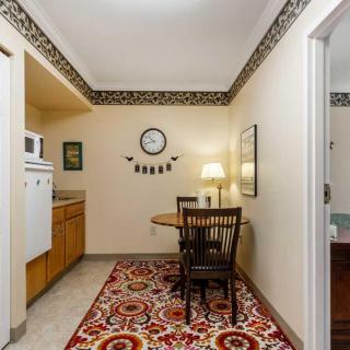 A cozy dining area with a table and chairs, adorned with a colorful rug and a wall clock.