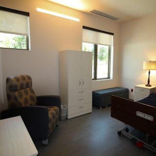 A well-lit healthcare room with a bed, armchair, and storage.