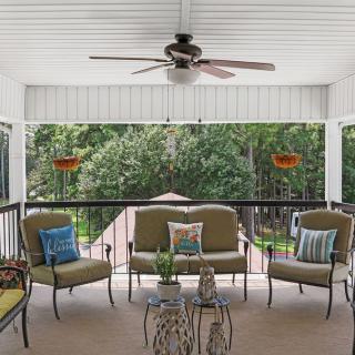 A cozy patio setup with comfortable seating and a ceiling fan overlooks a lush backyard.