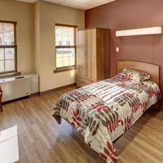 A cozy bedroom with a single bed, wooden flooring, and ample natural light.