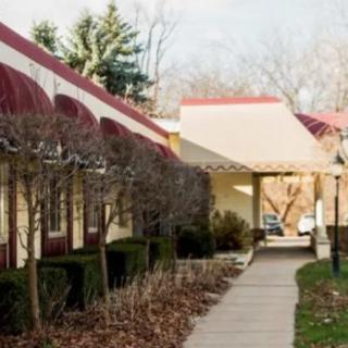 A walkway lined with trimmed bushes and trees, adjacent to a building with red awnings.