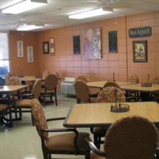 A spacious cafeteria with multiple tables and chairs arranged neatly, featuring wall decor and a neutral color scheme.