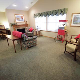 A cozy living room with a fireplace, sofa, chairs, and a popcorn machine by the window.
