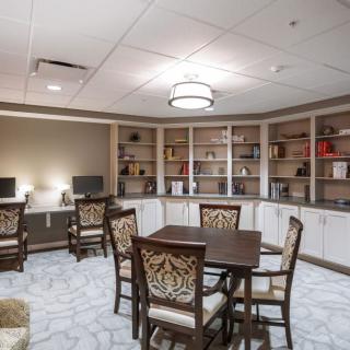 A cozy library room with bookshelves, computers, and several tables and chairs.