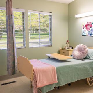 A serene hospital patient room featuring a neatly made bed, soft bedding, and large windows allowing natural light to fill the space.