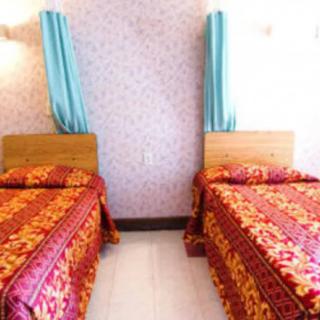 A cozy bedroom featuring two twin beds with vibrant bedding and blue curtains.