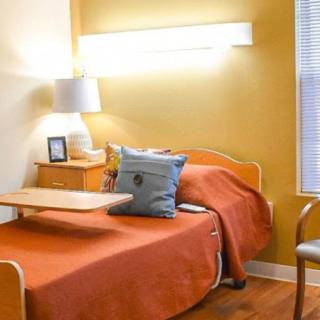 A cozy bedroom with a hospital bed featuring orange bedding, a bedside lamp, and wooden furniture.
