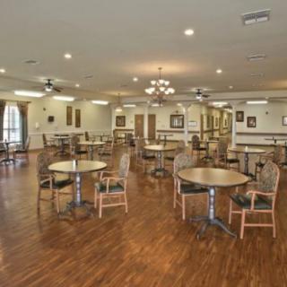 A spacious dining area featuring several round tables and chairs, with a hardwood floor and elegant chandeliers.