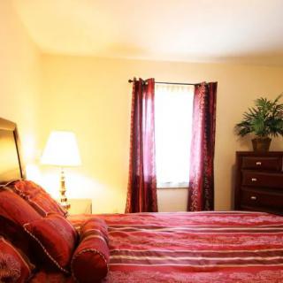 A cozy bedroom with a neatly made bed, warm lighting, and red curtains.