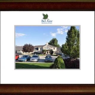 A picturesque view of Bel Aire Senior Living with cars parked in front and trees surrounding the building under a clear sky.
