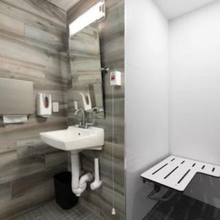 A modern, accessible bathroom with a wall-mounted sink and folding chair.