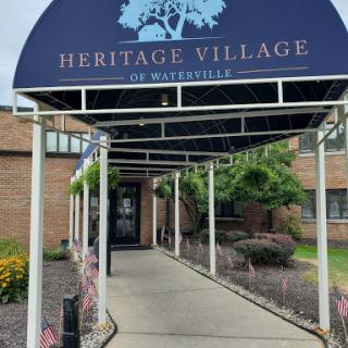 The entrance to Heritage Village in Waterville, featuring a welcoming awning and landscaped surroundings.