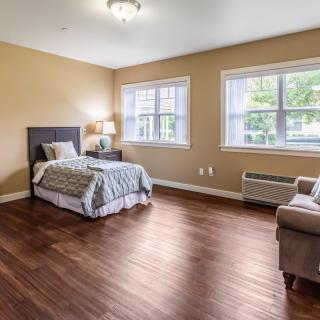 A spacious bedroom with a single bed, hardwood floors, and large windows letting in natural light.