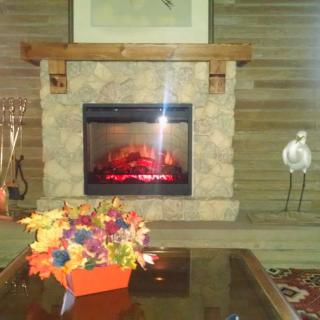 A cozy living room featuring a stone fireplace with an artificial fire, decorated with colorful flowers on the coffee table.