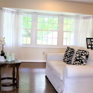 A bright and airy living room with a large window, white sofa, and geometric cushions.
