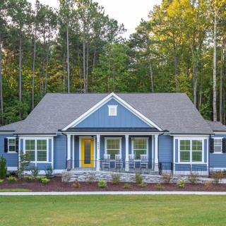 A charming blue house with a welcoming front porch and surrounded by trees.