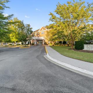 Entrance to a building surrounded by trees and a landscaped driveway.