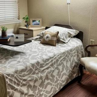 A cozy bedroom with a single bed, decorated with patterned bedding and pillows, alongside a wooden side table, chair, and lamp.