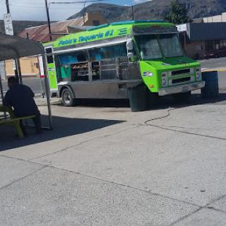 A vibrant green food truck parked in an urban setting, offering street food with a scenic mountain backdrop.