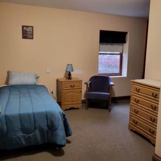 A minimalist bedroom with a single bed, dresser, and chair.