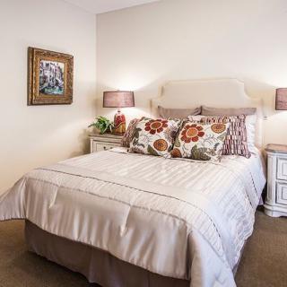 A cozy and well-decorated bedroom featuring a bed with floral pillows, bedside lamps, and a framed artwork on the wall.