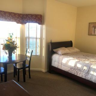 A cozy bedroom featuring a bed, a small table with chairs, and a bouquet of flowers by the window.