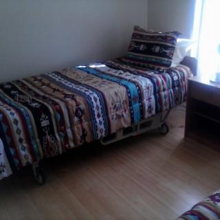 A cozy bedroom with a single bed covered in a patterned quilt next to a desk by the window.