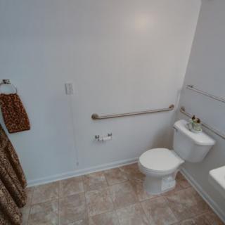 A bathroom featuring a toilet, sink, and grab bars for accessibility.