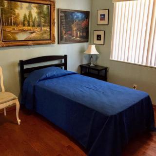 A cozy bedroom with a single bed and blue bedding, featuring wall art and a nightstand with a lamp.