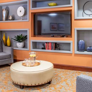 A modern living room with orange walls, featuring built-in shelves, a TV, and a stylish ottoman.