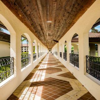 A beautifully symmetrical corridor with arched openings, a wooden ceiling, and patterned tiles, showcasing intricate play of sunlight and shadows.