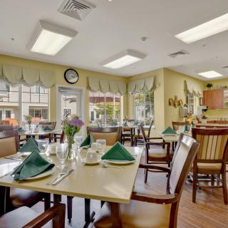A cozy dining room setup with neatly arranged tables, green napkins, and comfortable seating.