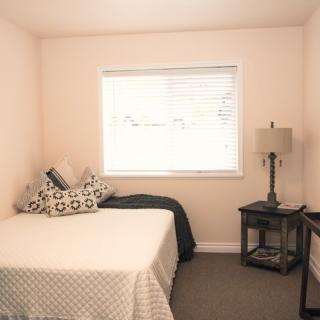 A minimalist bedroom with a bed, lamp, and window providing natural light.
