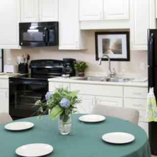 A modern kitchen with a round table set for four, featuring black appliances and white cabinetry.