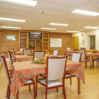 An indoor dining room with multiple tables and chairs, featuring tablecloths and wooden furniture.