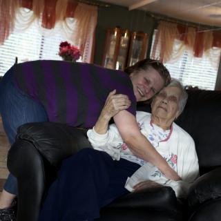 A young woman hugging an elderly woman on a sofa in the living room.