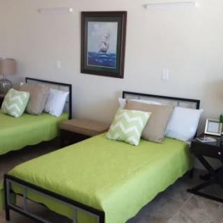 A cozy bedroom with two twin beds featuring green bedding and decorative pillows, complemented by a piece of artwork on the wall.
