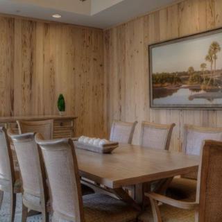 A cozy dining room with wooden walls, featuring a table and chairs, and a landscape painting on the wall.