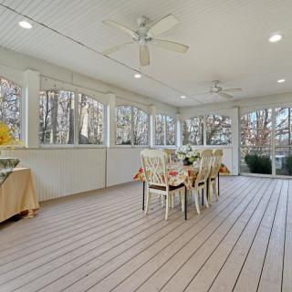 A bright sunroom featuring a dining table with chairs, surrounded by large windows and equipped with ceiling fans and wood flooring.