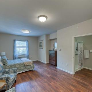 A cozy bedroom with a wooden floor, featuring a single bed, armchair, and an adjoining bathroom.