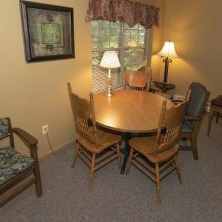 A cozy dining area with a round wooden table surrounded by chairs, softly lit by a lamp near the window.