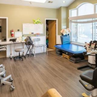 A bright and organized rehabilitation clinic workspace featuring medical equipment, desks, and chairs.